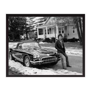 Puede incluir: Fotografía en blanco y negro de un coche descapotable negro clásico aparcado en una calle bordeada de nieve. Una persona se apoya en el coche. Una casa está al fondo.