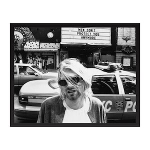 May include: Black and white photograph featuring a person with sunglasses and long blonde hair in front of a taxi. A sign above reads "MEN DON'T PROTECT YOU ANYMORE". The image is framed in black.
