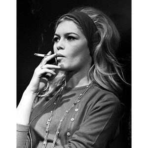 May include: Black and white photograph of a woman smoking a cigarette. She wears a dark headband, a button-down cardigan, and a long beaded necklace. The image is a portrait, with the woman's face in profile. The print size is 5x7 inches and 20x28 inches.