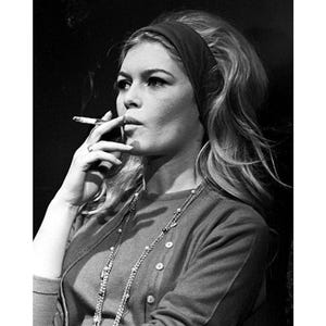 May include: Black and white photograph of a woman with long blonde hair wearing a dark headband, a cardigan, and a necklace. She is smoking a cigarette. The image includes the text "30x40 cm / 60x80 cm" and "12x16" / 24x32".