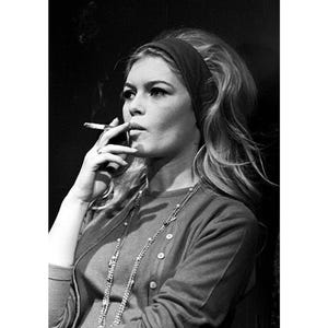May include: Black and white photograph of a woman smoking a cigarette. She wears a dark headband, a button-down cardigan, and a long necklace. The image includes size options: 4x6", 8x12", and 16x24".