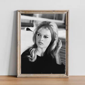 May include: Black and white framed portrait of a woman with blonde hair and a red headband. The woman is wearing a black top and looking off to the side. The image is in a wooden frame.