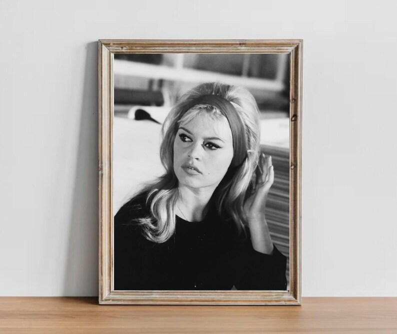 May include: Black and white framed portrait of a woman with blonde hair and a red headband. The woman is wearing a black top and looking off to the side. The image is in a wooden frame.