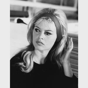 May include: Black and white photograph of a woman with blonde hair wearing a dark top and a headband. The image includes the text "13X18 cm / 50X70 cm" and "5x7" / 20x28".