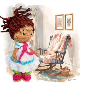 Könnte beinhalten: Eine handgefertigte Häkelpuppe mit braunen Haaren und einem weißen Kleid mit blauen und rosa Akzenten. Die Puppe steht in der Nähe eines hölzernen Schaukelstuhls mit einer rosa Decke. Zwei gerahmte Tierillustrationen hängen an der Wand.