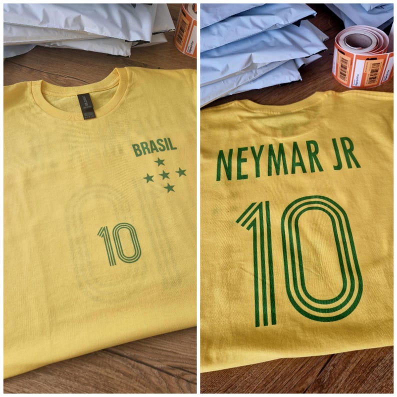 Puede incluir: Dos camisetas amarillas con texto y gr&aacute;ficos verdes. Una camiseta dice "BRASIL" con estrellas y el n&uacute;mero "10". La otra camiseta dice "NEYMAR JR" y el n&uacute;mero "10".