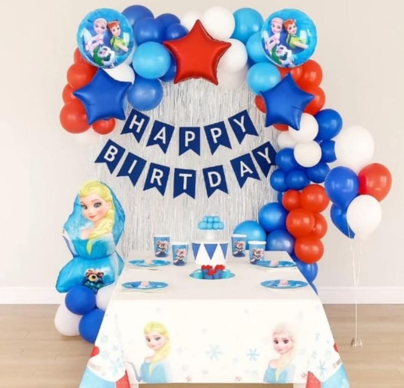 May include: A festive birthday party setup featuring a table with a themed tablecloth, cups, and plates. Balloons in red, white, and blue, along with star-shaped and character balloons, create an arch. A banner reads "Happy Birthday."