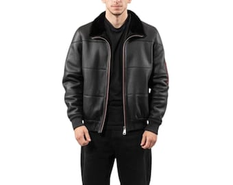 May include: Black leather bomber jacket with a black fur collar. The jacket has a zip-up front, ribbed cuffs, and a red stripe detail on the sleeve. The jacket is worn over a black shirt and black pants.