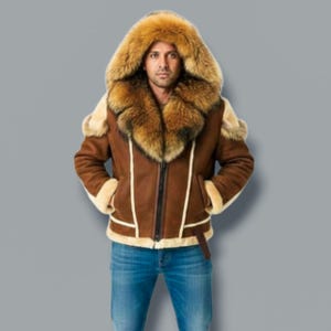 Puede incluir: Chaqueta de borrego marrón con capucha y cuello forrados de piel. La chaqueta tiene cremallera frontal, bolsillos laterales y detalle de cinturón en la cintura. Los puños y el forro interior son de un tono marrón más claro. La persona lleva vaqueros azules.