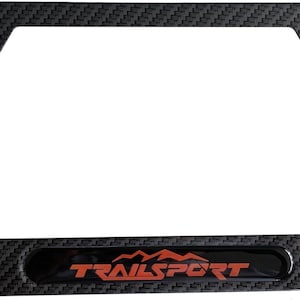 Puede incluir: Marco de matrícula negro con textura de fibra de carbono. El marco tiene la palabra "TRAILSPORT" en letras naranjas. El marco tiene cuatro orificios de montaje.