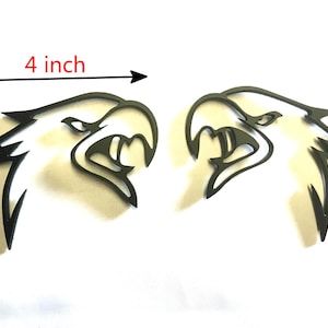 May include: Two black eagle head emblems. Each emblem is 4 inches wide and 3.25 inches tall. The eagles have open beaks and sharp details, suitable for automotive or decorative use.