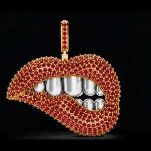 May include: A gold pendant in the shape of lips, encrusted with red gemstones. The teeth are silver-colored. The pendant has a gold bail at the top for a chain.