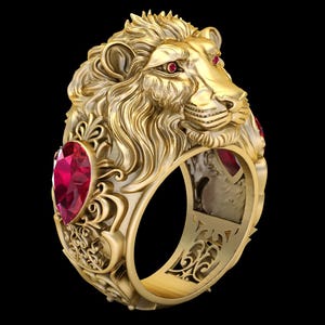 Könnte beinhalten: Ein goldfarbener Ring mit einem detaillierten Löwenkopf, roten Edelsteinaugen und Rubinen an den Seiten. Der Ring hat ein aufwendiges, geschnitztes Design und ist vor schwarzem Hintergrund platziert.