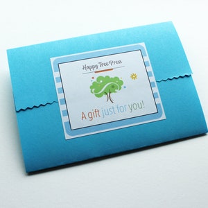 The packaging for a present which includes a blue envelope with a white label that says 'Happy Tree Press' and it's logo of a green tree with brown branches and a yellow sun. The label also says 'A gift just for you!'