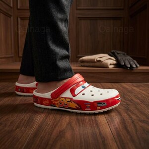 Puede incluir: Zuecos blancos y rojos de Lightning McQueen con una correa roja. Los zuecos presentan el n&uacute;mero 95 y gr&aacute;ficos de Lightning McQueen. Los zapatos son de estilo sin cordones y tienen una puntera redondeada.