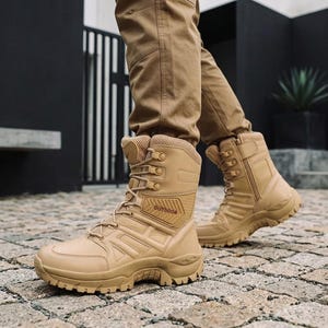 Puede incluir: Un par de botas tácticas de color beige con diseño de caña alta, cordones, cremalleras laterales y suela reforzada. El lateral de cada bota muestra la palabra OUTDOOR en fuente oscura, con un panel texturizado y cuello acolchado.