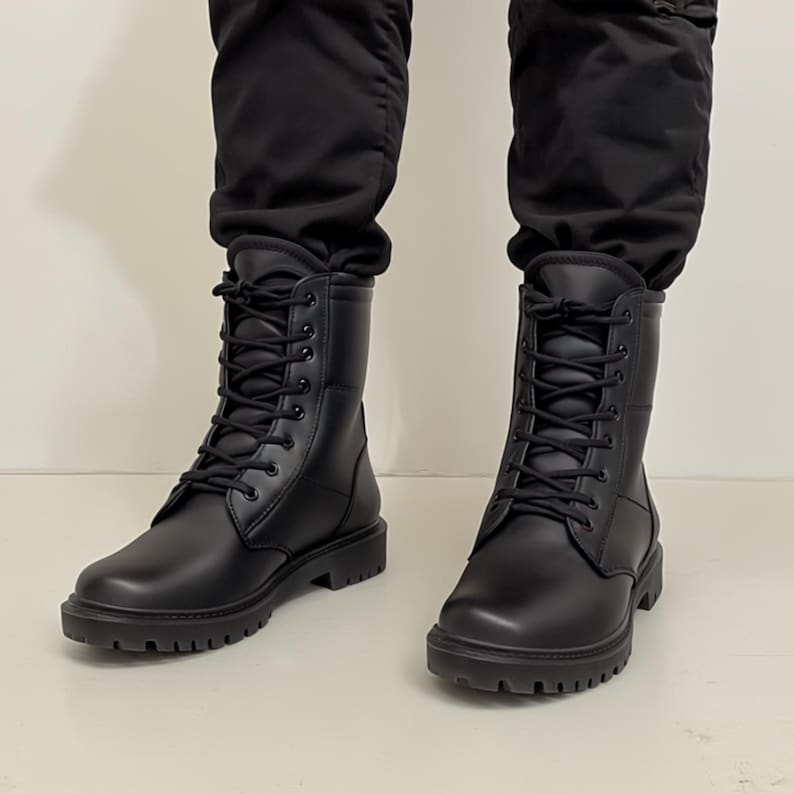 Puede incluir: Un par de botas de combate negras con cordones. Las botas tienen una puntera redondeada y una suela gruesa. Las botas est&aacute;n hechas de un material liso y se llevan con pantalones negros.