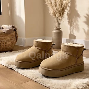 Op de afbeelding: Een paar bruinbeige enkellaarsjes met een plateauzool. De laarzen hebben een su&egrave;de-achtige textuur en een pluizig, cr&egrave;mekleurig interieur. De laarzen worden getoond op een wit tapijt.