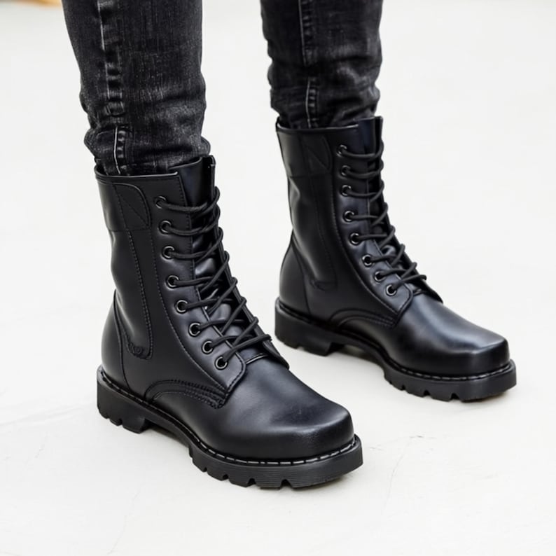 Puede incluir: Botas de combate de cuero negro con dise&ntilde;o de cordones. Las botas tienen una puntera redondeada y una suela gruesa. Las botas se llevan con vaqueros negros.