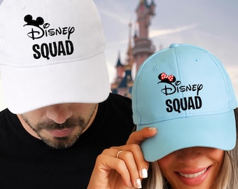May include: Two baseball caps, one white and one light blue, each with the text "Disney SQUAD" in black. The white cap has a black Mickey Mouse silhouette. The light blue cap has a Minnie Mouse silhouette with a red bow.