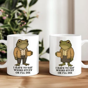 May include: Two white ceramic mugs with a cartoon frog design. The frog wears a tan cardigan and holds a coffee cup. Text on the mugs reads "I HAVE TO SAY WEIRD STUFF OR I'LL DIE".