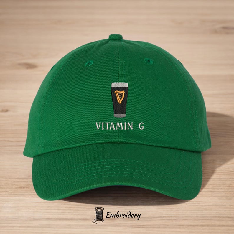 May include: Green baseball cap with the embroidered text "VITAMIN G" below a graphic of a pint of stout with a golden harp. The cap has a curved brim and a top button.
