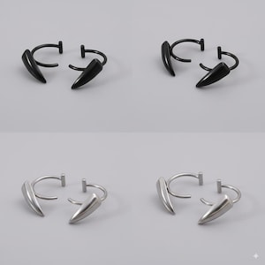 May include: Four pairs of earrings, each featuring a curved hoop design with a pointed, fang-like charm. Two pairs are black, and two are silver, all set against a neutral gray background.
