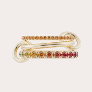 May include: Three gold rings interlocked, featuring a gradient of gemstones. The top ring has orange gemstones, the middle is plain gold, and the bottom ring displays a spectrum of colors from yellow to red. The rings are connected by gold links.