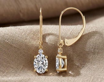 May include: A pair of gold-coloured leverback earrings. Each earring features a large, oval-cut, clear gemstone suspended below a smaller, round gemstone. The earrings are set in a gold-coloured metal and are displayed against a neutral background.