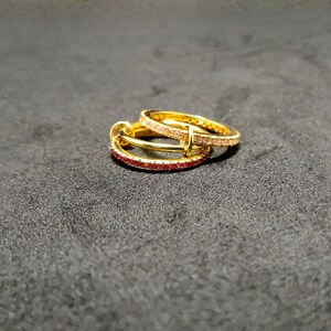 May include: Two gold-colored hoop earrings with small, embedded gemstones. One earring features red gemstones, while the other has pink gemstones. The earrings are stacked on top of each other, creating a layered effect.