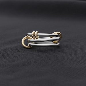 Op de afbeelding: Een zilveren en gouden ring met een uniek ontwerp. De ring heeft meerdere zilveren banden die worden samengehouden door gouden accenten. De gouden elementen omvatten kleine verbindingsringen en grotere cirkelvormige vormen.