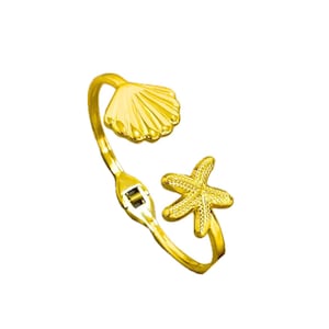 May include: A gold-coloured adjustable ring with a seashell and starfish design. The ring has a hinged design with a seashell on one end and a starfish on the other. The ring is made of a shiny, metallic material.
