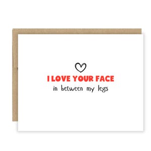 May include: A white greeting card with a brown envelope. The card has the text "I LOVE YOUR FACE" in red, and "in between my legs" in black, with a black heart above the text.