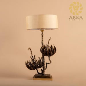 Peut inclure: Une lampe de table d&eacute;corative avec un abat-jour beige et une base florale de couleur bronze. La base pr&eacute;sente des motifs complexes et stylis&eacute;s de fleurs et de tiges. La lampe est con&ccedil;ue pour une utilisation en int&eacute;rieur.