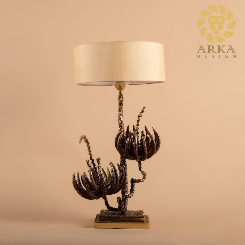 Peut inclure: Une lampe de table d&eacute;corative avec un abat-jour beige et une base florale de couleur bronze. La base pr&eacute;sente des motifs complexes et stylis&eacute;s de fleurs et de tiges. La lampe est con&ccedil;ue pour une utilisation en int&eacute;rieur.