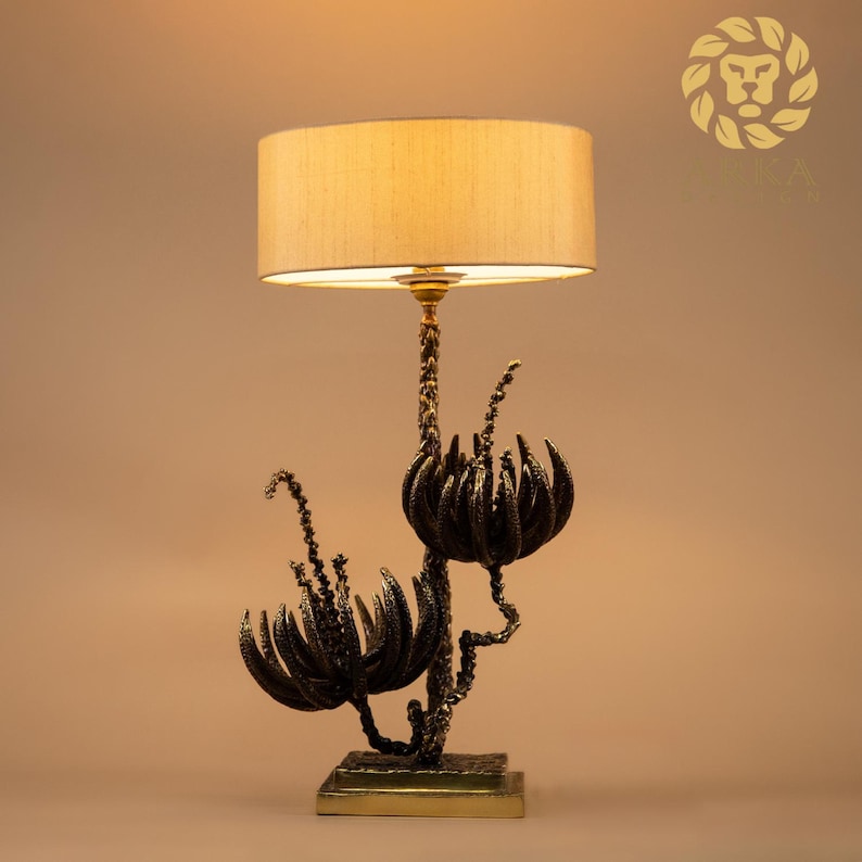 Peut inclure: Une lampe de table d&eacute;corative avec un abat-jour beige et une base florale de couleur bronze. La base pr&eacute;sente des motifs stylis&eacute;s de fleurs et de tiges. La lampe est con&ccedil;ue pour fournir un &eacute;clairage d'ambiance et convient &agrave; un salon ou une chambre.