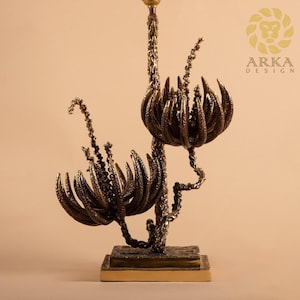 Peut inclure: Une sculpture d&eacute;corative de couleur bronze avec un motif floral. La sculpture pr&eacute;sente de multiples structures en forme de fleurs avec des p&eacute;tales et des tiges textur&eacute;s et d&eacute;taill&eacute;s. La base est de forme rectangulaire avec une bordure dor&eacute;e. Le logo "ARKA DESIGN" est visible.