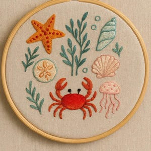 Könnte beinhalten: Gesticktes Kunstwerk in einem Holzreifen, das Meereslebewesen darstellt. Das Design umfasst einen Seestern, eine Krabbe, Muscheln und Seetang in Orange, Rot, Grün und Rosa. Der Reifen ist aus Holz.