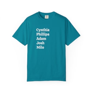 May include: Teal-colored t-shirt with the names Cynthia, Phillipa, Adam, Josh, and Milo printed in white. The shirt is a crew neck style and appears to be made of a soft, comfortable material. The names are vertically aligned.