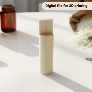 May include: A light beige cylindrical object with a rectangular top, labelled "Digital file for 3D printing." A brown glass jar and a bag of white granules are in the background. The object casts a shadow on the white surface.