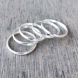 May include: A set of five thin, polished silver-colored metal rings arranged in a slightly overlapping, staggered formation. Each ring features a smooth, rounded band with a reflective surface, creating a uniform and simple circular design.