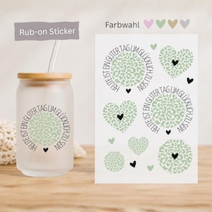 Könnte beinhalten: Ein mattiertes Glas mit Bambusdeckel und Trinkhalm, verziert mit einem kreisförmigen salbeigrünen Leopardenmuster und dem Text "Heute ist ein guter Tag um glücklich zu sein" sowie einem Bogen mit passenden Rub-on-Stickern mit Herzmotiven.