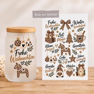 Könnte beinhalten: Ein mattiertes Glas mit Holzdeckel und ein Bogen mit Rub-on-Stickern im Leopardenmuster-Weihnachtsdesign, darunter Christbaumkugeln, ein Dala-Pferd, ein Wichtel und deutscher Text wie Frohe Weihnachten und Winter Wonderland.