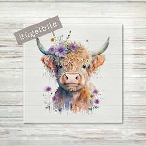 Könnte beinhalten: Ein quadratisches Bügelbild mit einer Aquarellillustration eines flauschigen Hochlandrindes mit langen Hörnern. Das Rind ist mit violetten und gelben Blumen auf dem Kopf und am unteren Rand verziert. Der Text "Bügelbild" steht auf einem grauen Banner.