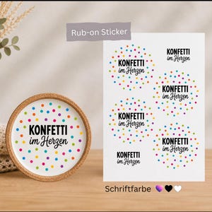 Könnte beinhalten: Ein Bogen mit Rub-on-Stickern und ein runder Untersetzer mit dem schwarzen Schriftzug "KONFETTI im Herzen", umgeben von einem bunten Muster aus kleinen blauen, gelben, rosafarbenen und grünen Punkten. Der Bogen enthält mehrere Motive.