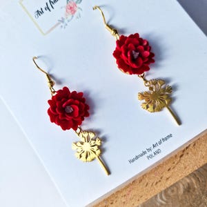 Może przedstawiać: Ręcznie robione kolczyki z czerwonymi zawieszkami w kształcie kwiatów i złotymi zawieszkami w kształcie dmuchawców. Kolczyki zawieszone są na złotych haczykach. Tekst "Art of frame" jest widoczny w tle. Wyprodukowano w Polsce.