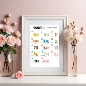 Könnte beinhalten: Ein gerahmtes Hangul-Tierposter mit farbenfrohen koreanischen Wörtern und ihren englischen Übersetzungen. Der weiße Rahmen steht auf einer weißen Oberfläche, mit rosa Rosen in einer Vase links und weißen Blumen in einer Vase rechts.