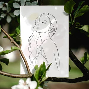 Op de afbeelding: Een minimalistische lijntekening van een vrouw met gesloten ogen en vloeiend haar. Het kunstwerk is in zwart op een witte achtergrond met zachte aquarelwashes van roze en geel. De print wordt omlijst door een natuurlijke buitenomgeving met groene bladeren en witte bloemen.