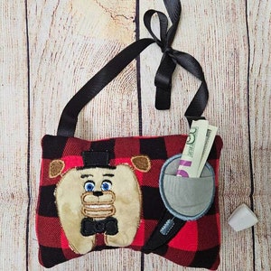 May include: A red and black plaid fabric pouch with a black strap and a black bow. The pouch features an embroidered image of a cartoon character with a top hat, bow tie, and a large smile. The pouch has a small pocket on the side with a bill sticking out.