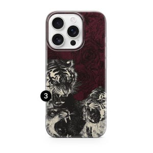 May include: A phone case featuring a detailed illustration of three roaring tigers in black and white. The background is a dark red with a subtle rose pattern. The case has a clear border and a camera cutout.